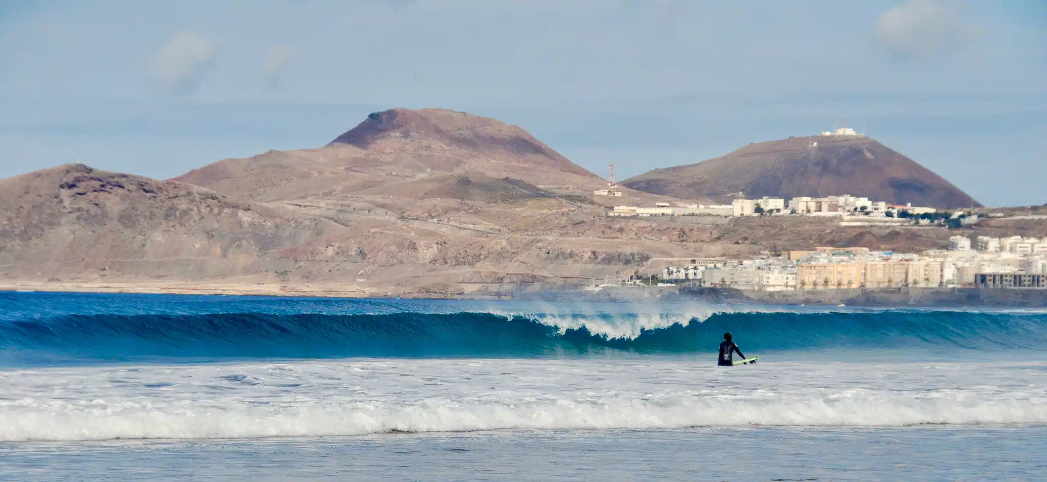 A human is surfing with mountains in background