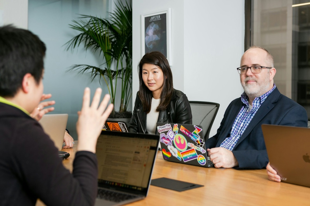 An engineer explaining a technical decision to two colleagues across a meeting table